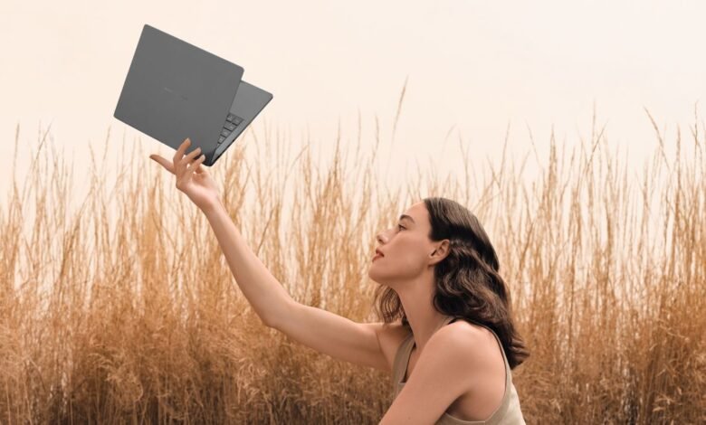 A woman holding up an Asus laptop in a field of wheat