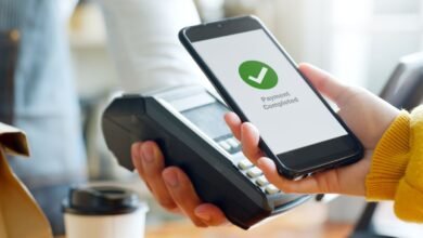 A hand making a contactless payment with a smartphone at a shop terminal