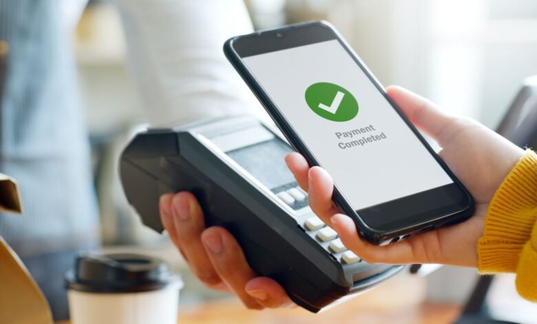 A hand making a contactless payment with a smartphone at a shop terminal